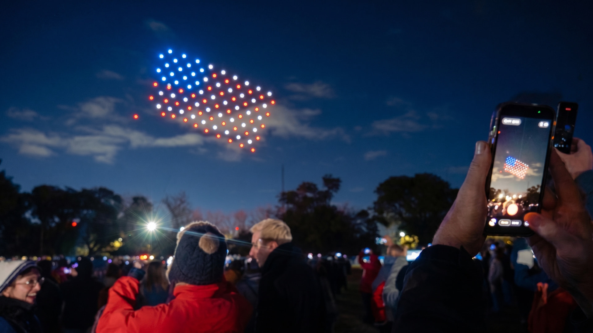 Público fotografiando la bandera de Estados Unidos formada por drones