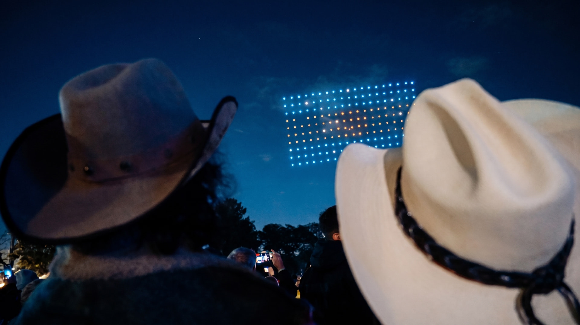 Público con sombreros mirando una formación de drones en el cielo