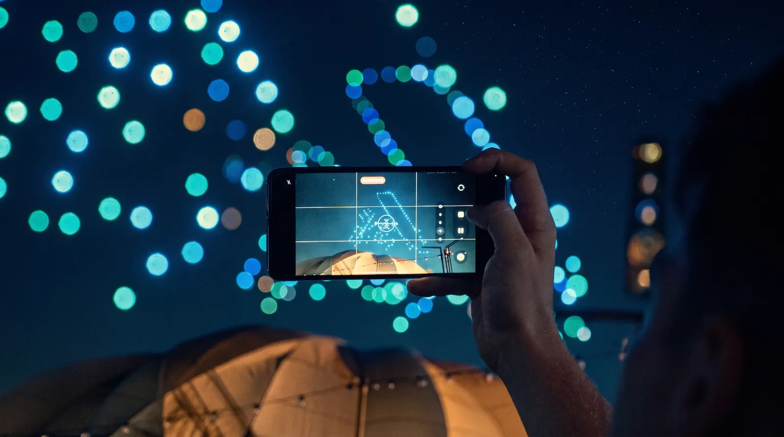 Espectador fotografiando con su celular un show de drones en el cielo nocturno